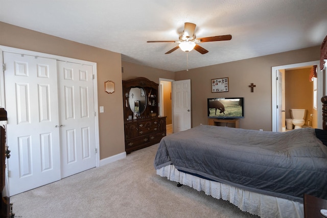 bedroom featuring baseboards, a ceiling fan, light colored carpet, ensuite bath, and a closet