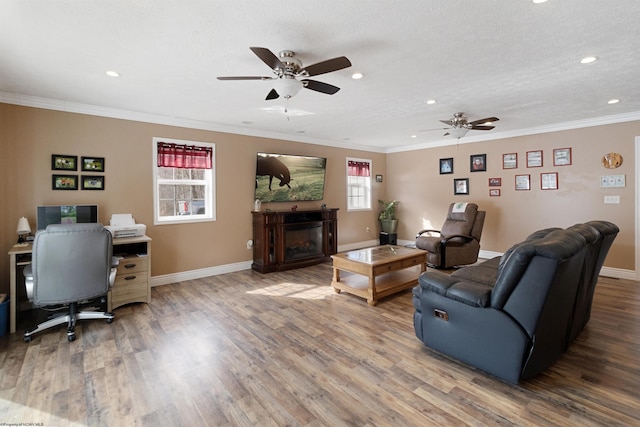 living area with ornamental molding, wood finished floors, a glass covered fireplace, and baseboards