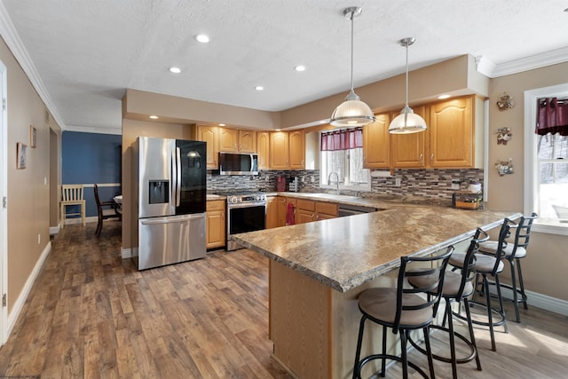 kitchen with a peninsula, a breakfast bar area, stainless steel appliances, and decorative light fixtures