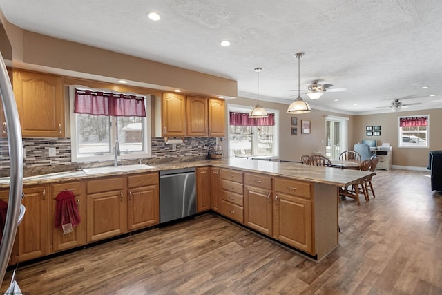 kitchen with stainless steel appliances, a peninsula, a sink, hanging light fixtures, and light countertops