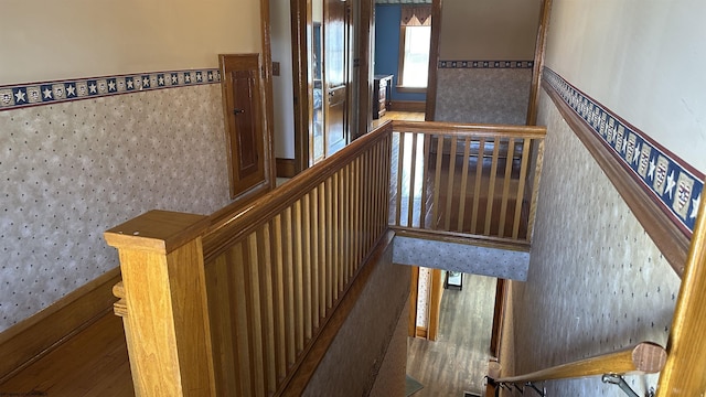 staircase with wallpapered walls, wood finished floors, and wainscoting