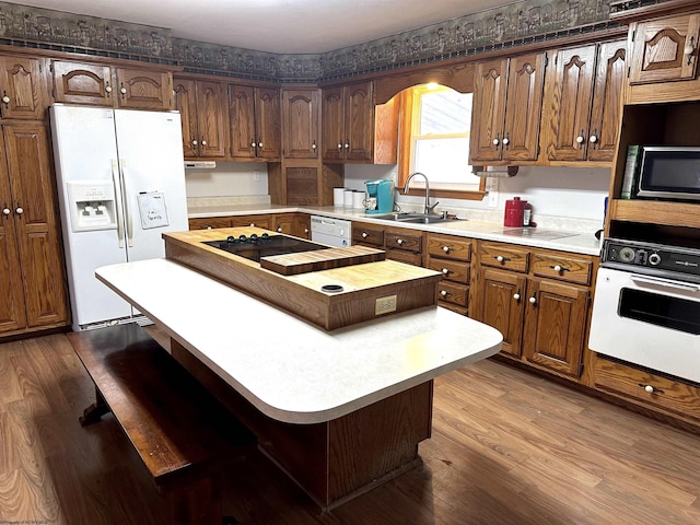 kitchen with wood finished floors, light countertops, white appliances, and a sink