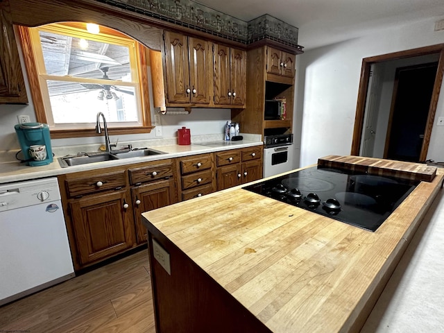 kitchen with black appliances, butcher block countertops, a sink, and wood finished floors