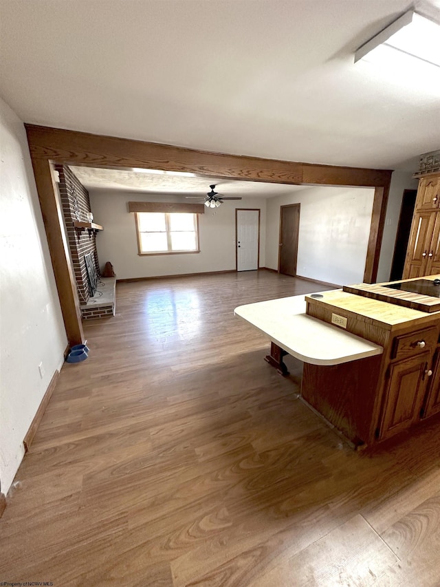 unfurnished living room with a ceiling fan, a fireplace, light wood-style flooring, and baseboards