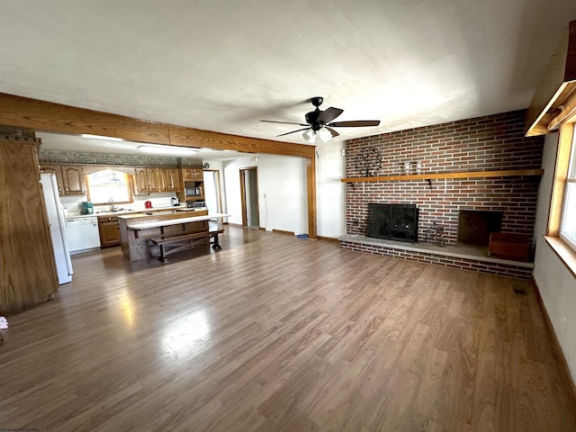 unfurnished living room featuring dark wood finished floors, a ceiling fan, a brick fireplace, a sink, and beamed ceiling