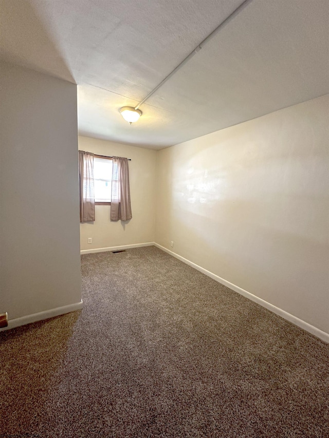 empty room featuring a textured ceiling, dark carpet, visible vents, and baseboards