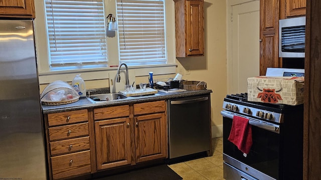 kitchen featuring stainless steel appliances, dark countertops, brown cabinetry, and a sink