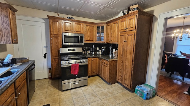 kitchen featuring an ornate ceiling, stainless steel appliances, brown cabinets, dark countertops, and glass insert cabinets