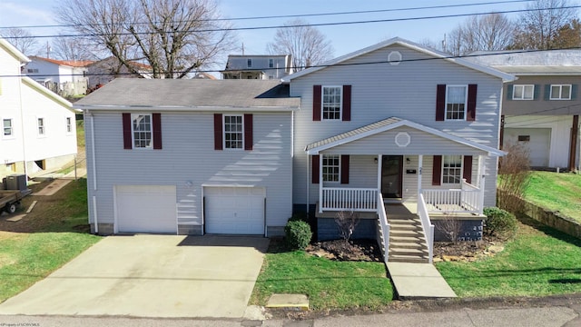 split level home featuring an attached garage, covered porch, concrete driveway, and a front yard