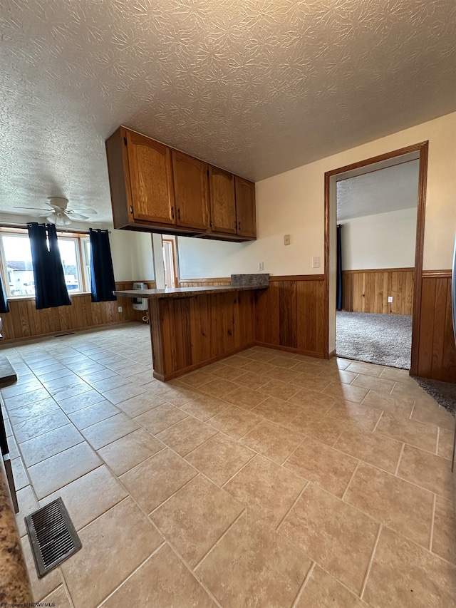 kitchen featuring brown cabinets, a wainscoted wall, visible vents, wooden walls, and a peninsula