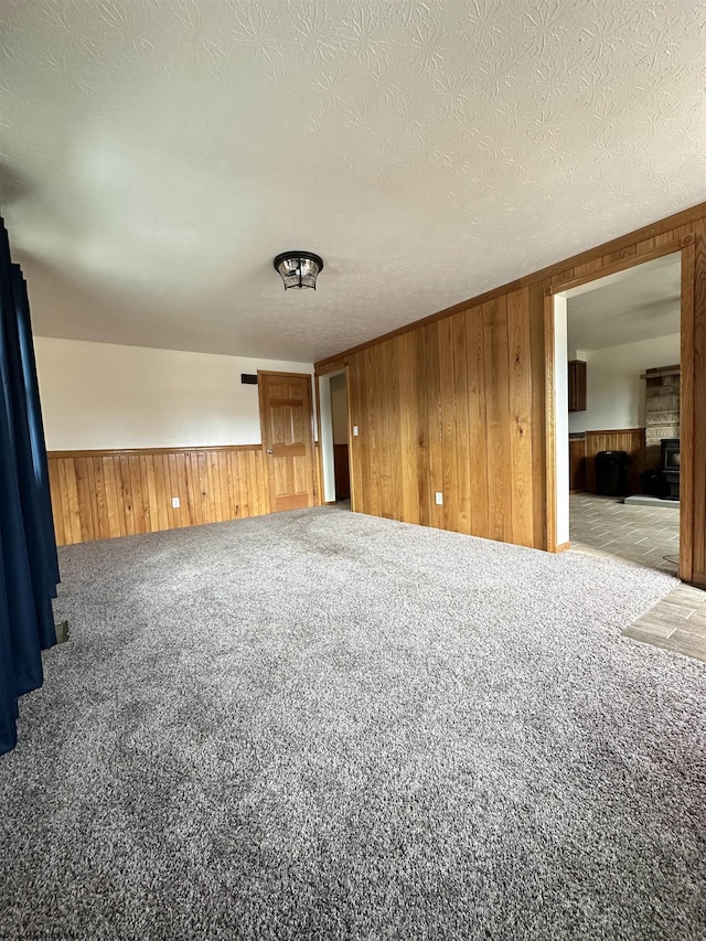 carpeted spare room featuring a wainscoted wall, wood walls, and a textured ceiling