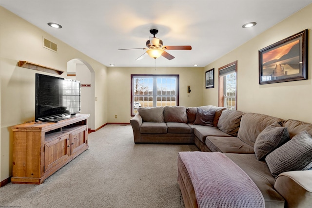 living room featuring light carpet, baseboards, visible vents, arched walkways, and ceiling fan