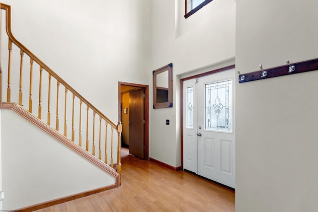 entrance foyer with a high ceiling, baseboards, stairway, and light wood finished floors