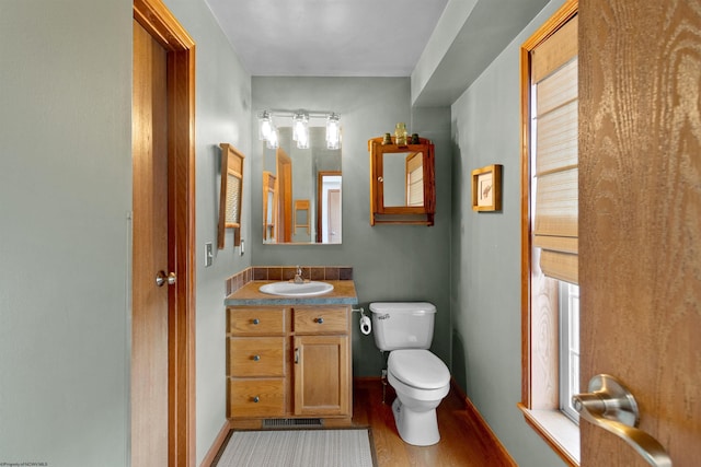 half bath featuring baseboards, visible vents, toilet, wood finished floors, and vanity