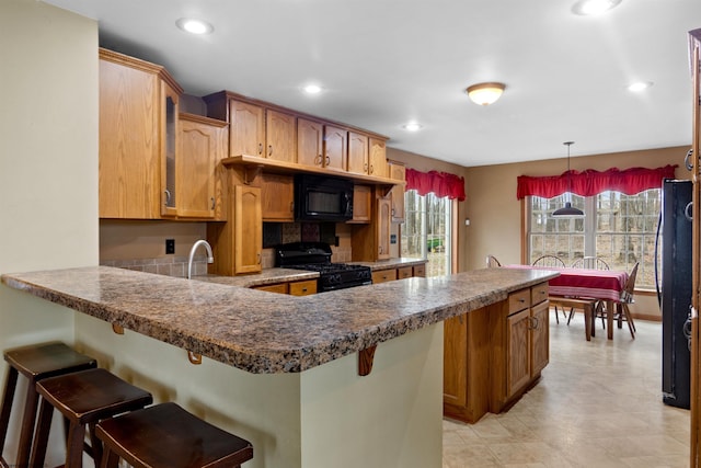 kitchen featuring black appliances, a breakfast bar area, a peninsula, and recessed lighting