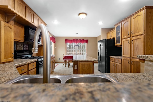 kitchen featuring a center island, black appliances, brown cabinetry, glass insert cabinets, and pendant lighting