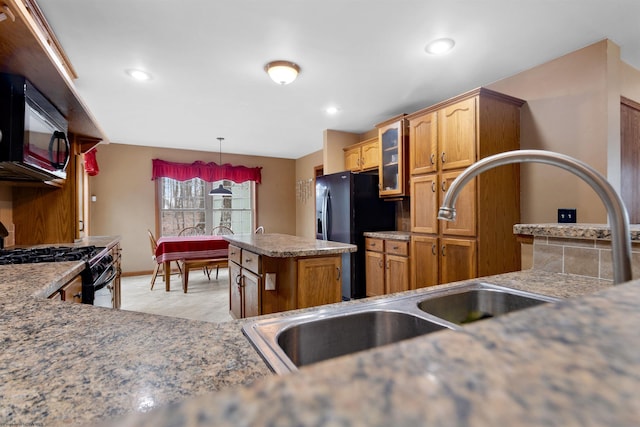 kitchen with a sink, brown cabinets, a center island, black appliances, and glass insert cabinets