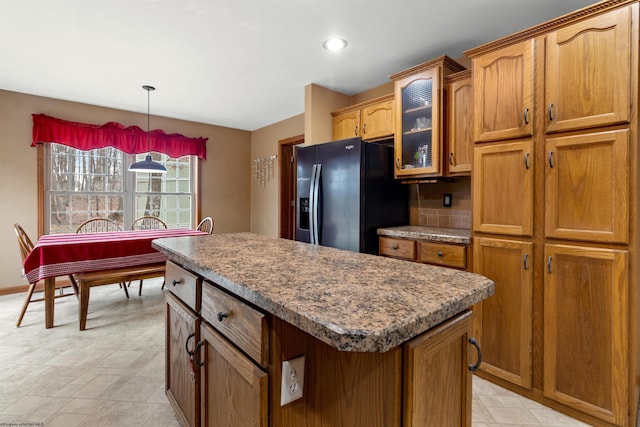 kitchen featuring a kitchen island, black refrigerator with ice dispenser, brown cabinetry, dark countertops, and glass insert cabinets