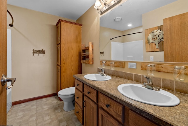 full bathroom with toilet, double vanity, baseboards, and a sink