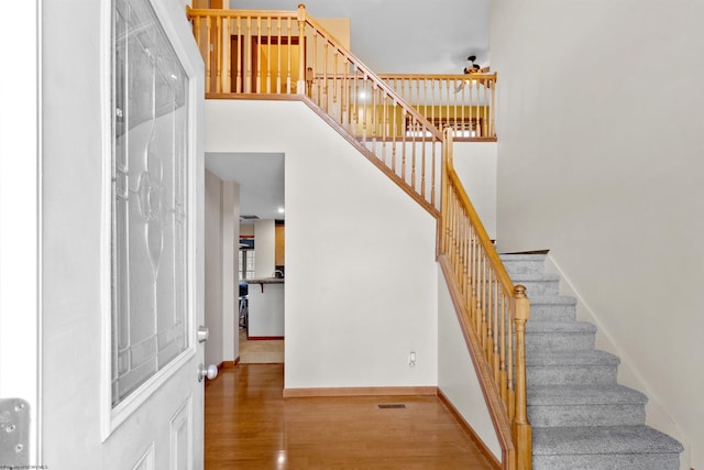 stairway featuring a towering ceiling, visible vents, baseboards, and wood finished floors