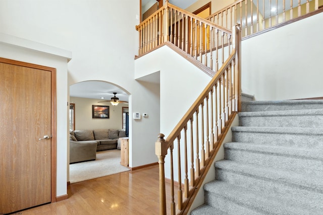 stairs with arched walkways, a towering ceiling, baseboards, and wood finished floors