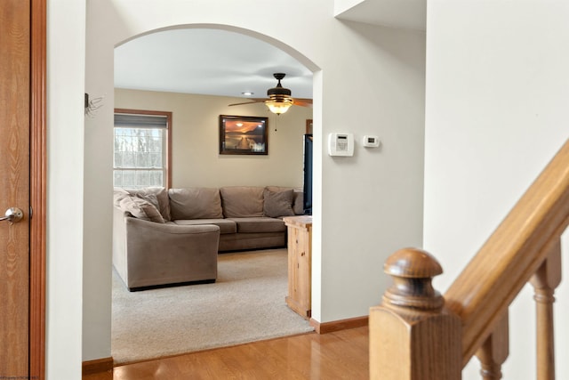 living room featuring light wood-style floors, ceiling fan, arched walkways, and baseboards