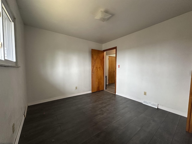 spare room with dark wood finished floors, visible vents, and baseboards