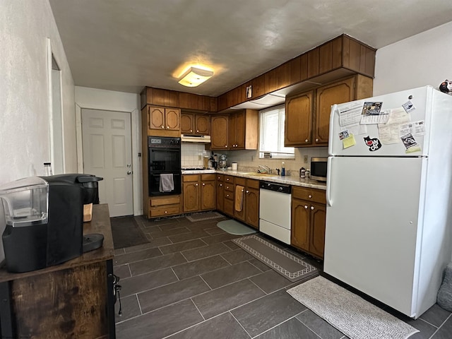 kitchen featuring under cabinet range hood, white appliances, light countertops, tasteful backsplash, and brown cabinetry