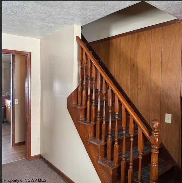 stairs with a textured ceiling, carpet flooring, and baseboards