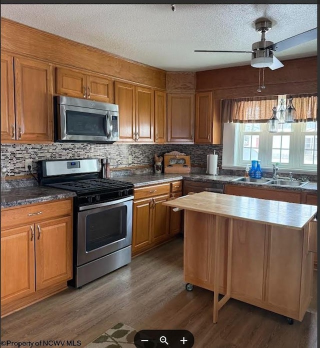 kitchen featuring wood finished floors, appliances with stainless steel finishes, brown cabinetry, and a sink