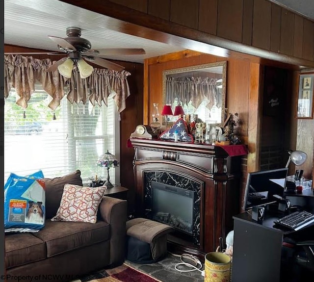 sitting room featuring wood walls, ceiling fan, and a premium fireplace