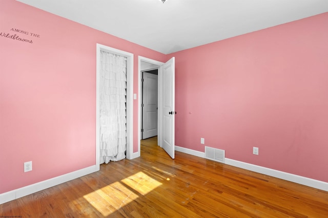 spare room featuring wood finished floors, visible vents, and baseboards