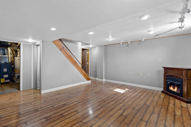 finished basement with stairs, a glass covered fireplace, track lighting, and wood finished floors