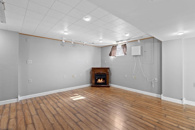 below grade area featuring a warm lit fireplace, track lighting, wood finished floors, and baseboards