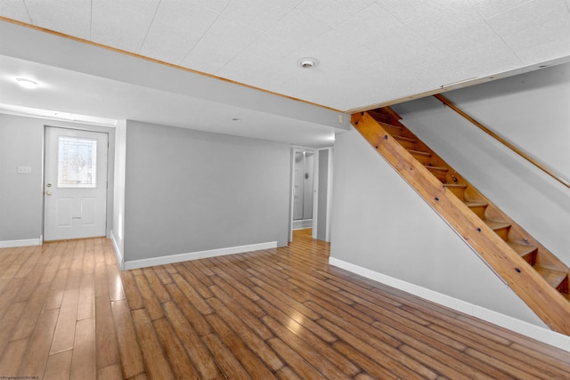 unfurnished living room with stairs, wood finished floors, and baseboards