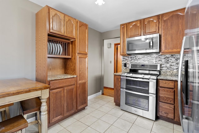 kitchen with light stone counters, stainless steel appliances, tasteful backsplash, brown cabinetry, and light tile patterned flooring