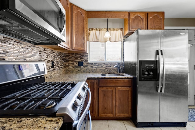 kitchen with light tile patterned floors, brown cabinetry, a sink, stainless steel appliances, and backsplash