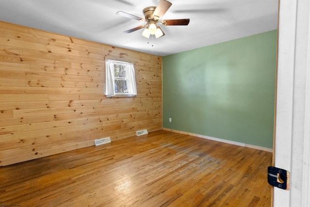 unfurnished room featuring ceiling fan, wooden walls, visible vents, and wood finished floors