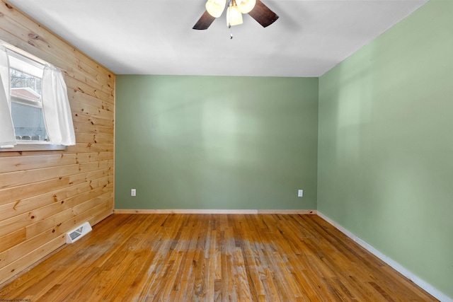 spare room featuring baseboards, hardwood / wood-style flooring, visible vents, and wooden walls