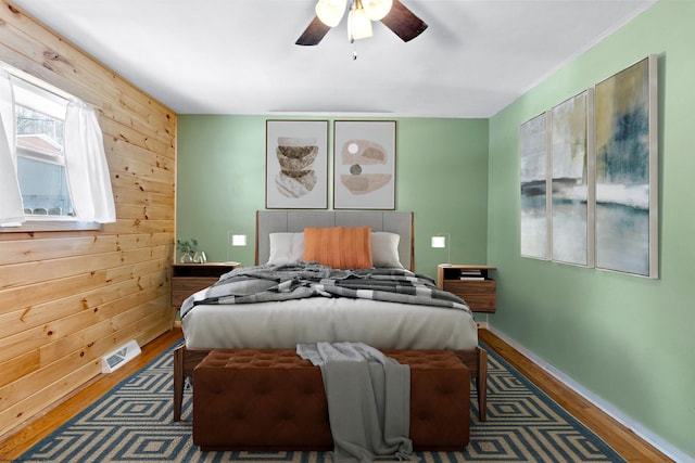 bedroom with visible vents, ceiling fan, wooden walls, wood finished floors, and baseboards