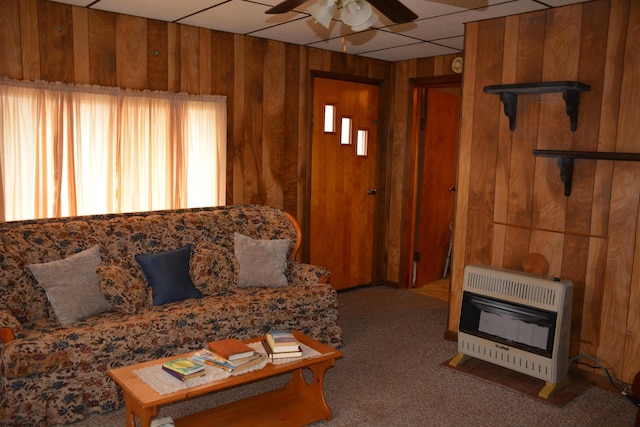 carpeted living room featuring heating unit, wooden walls, and a ceiling fan