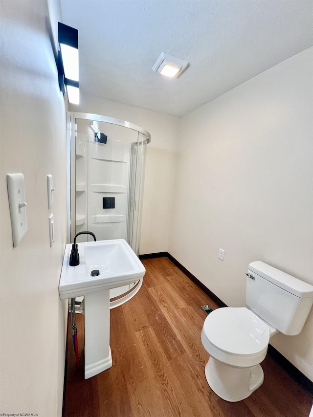 bathroom with toilet, a stall shower, baseboards, and wood finished floors