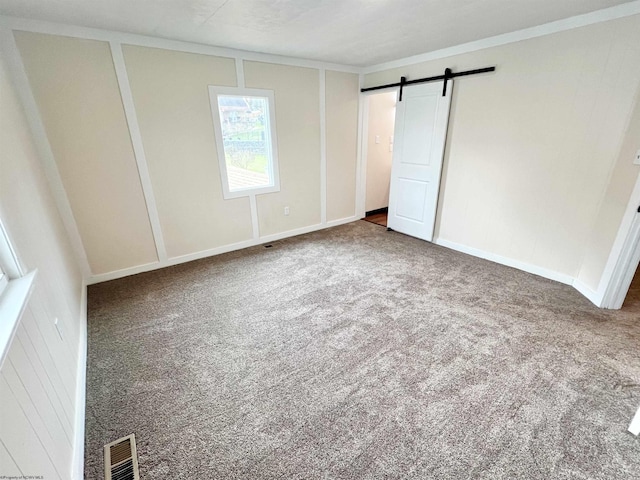 unfurnished bedroom featuring carpet floors, a barn door, visible vents, and ornamental molding