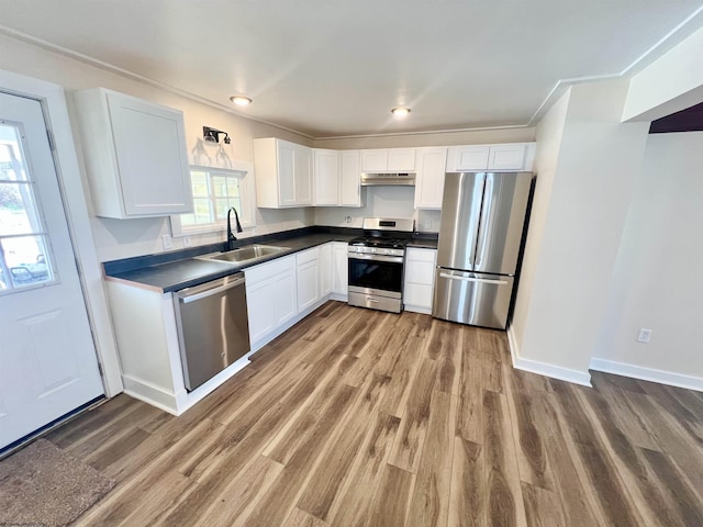 kitchen with dark countertops, wood finished floors, stainless steel appliances, white cabinetry, and a sink