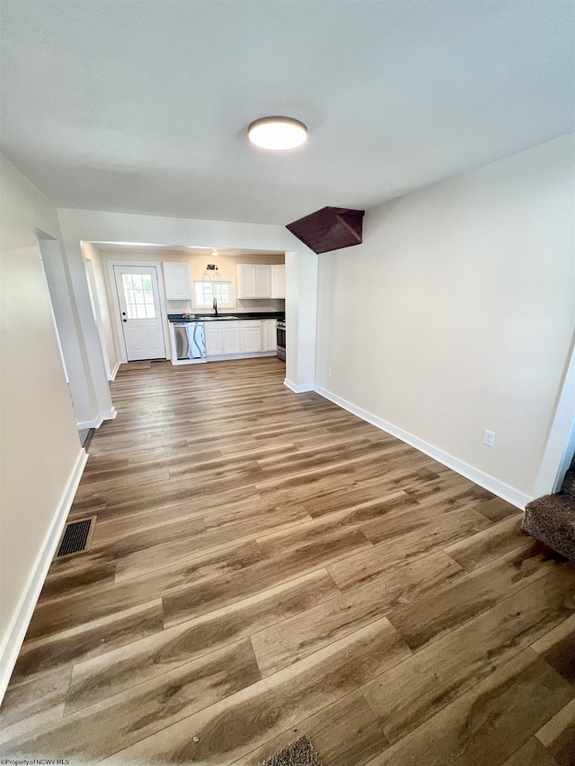 unfurnished living room with visible vents, a sink, baseboards, and wood finished floors