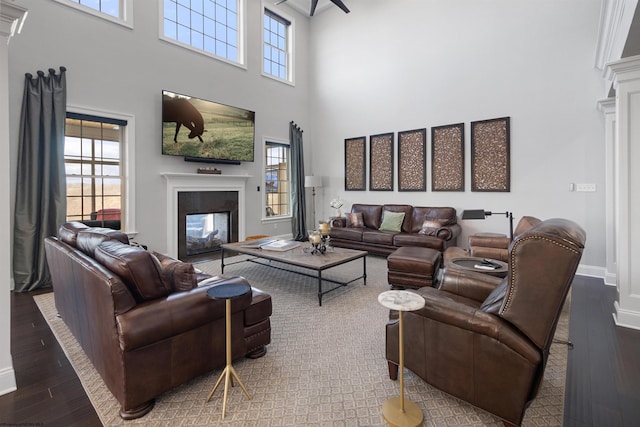 living area featuring wood finished floors, a towering ceiling, a multi sided fireplace, baseboards, and decorative columns