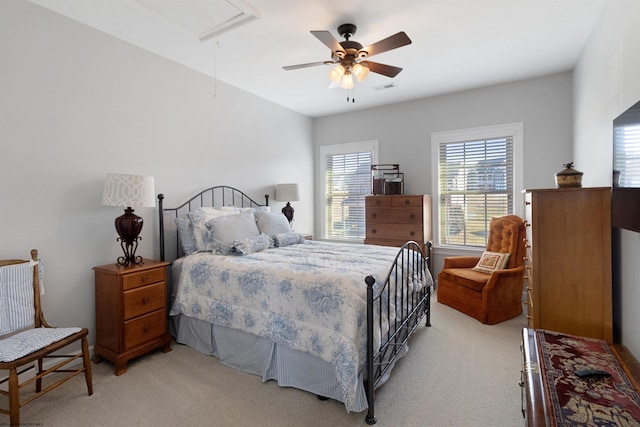 bedroom featuring attic access, light colored carpet, visible vents, and a ceiling fan