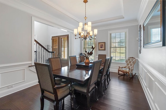 dining space featuring a decorative wall, dark wood-style flooring, stairs, ornamental molding, and a raised ceiling