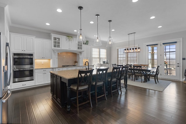 kitchen with dark wood-style floors, appliances with stainless steel finishes, light stone counters, and ornamental molding