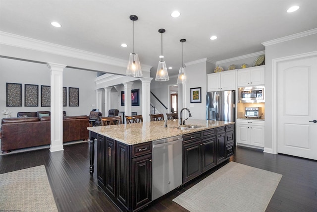 kitchen featuring stainless steel appliances, a sink, open floor plan, a kitchen bar, and ornate columns